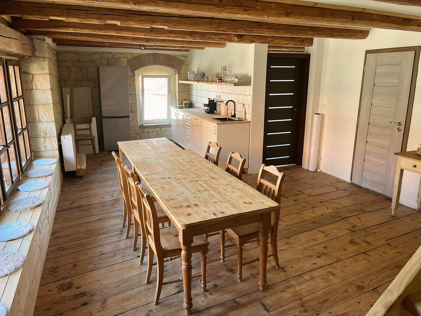 Dlouhý stůl u opukové zdi a kuchyňská linka